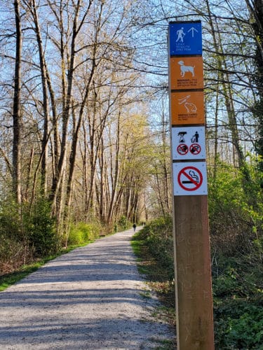 A picture of a trail with trail signs designating it an off-leash area next to it.
