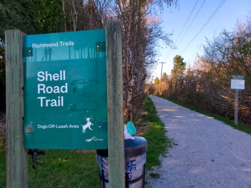 A picture of the shell road trail sign with the trail in the background
